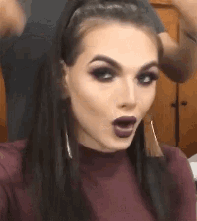 a woman with purple lipstick is making a surprised face while getting her hair done .