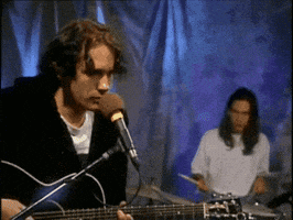 a man playing a guitar and singing into a microphone while another man plays drums