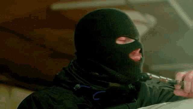 a man wearing a black ski mask is holding a gun .