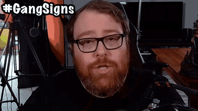 a man with glasses and a beard has the hashtag #gangsigns written above him