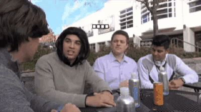 a group of men are sitting at a table with a can of orange soda in front of them