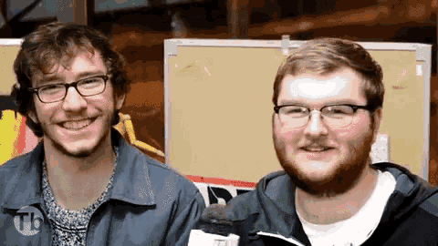 two men are smiling in front of a bulletin board that says tb