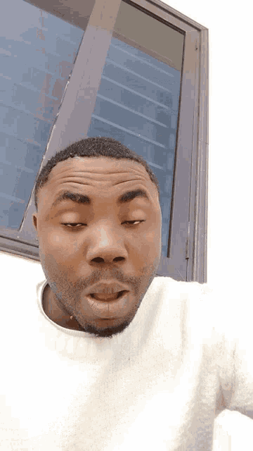 a man wearing a white sweater is making a funny face in front of a window