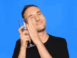 a man in a black shirt is holding a wine glass and rubbing his eyes .