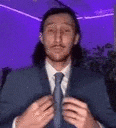 a man in a suit and tie is adjusting his tie in front of a purple background .