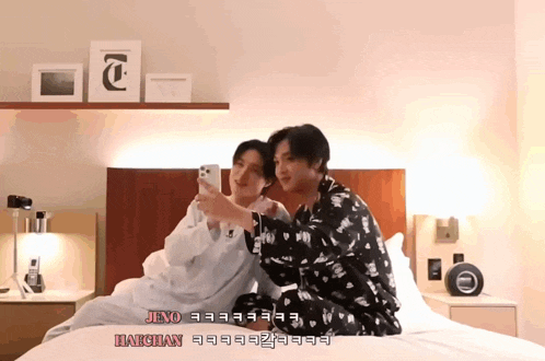 two men are sitting on a bed and one of them is taking a picture