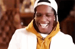 a close up of a man wearing a white hat and a yellow hoodie laughing .
