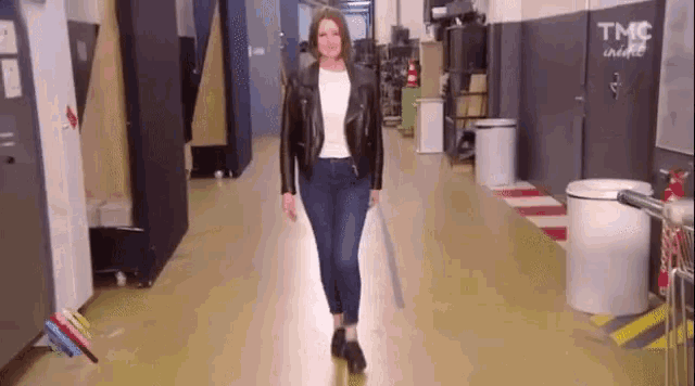 a woman in a leather jacket and jeans is walking down a hallway holding a sword .