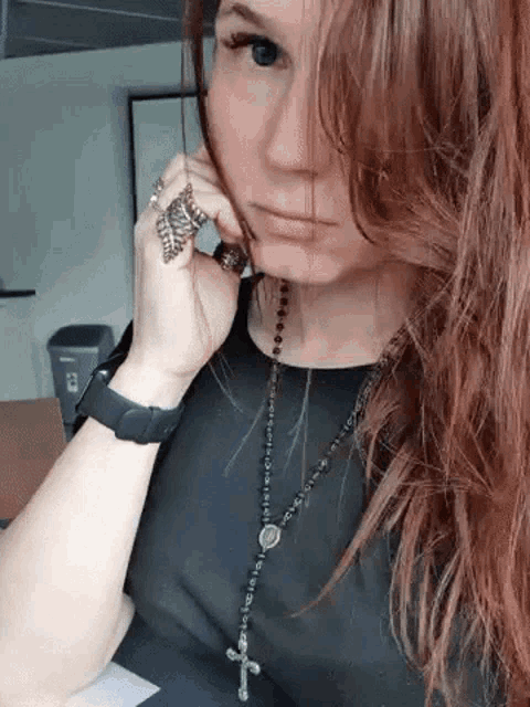 a woman wearing a black shirt and a rosary necklace is talking on a cell phone