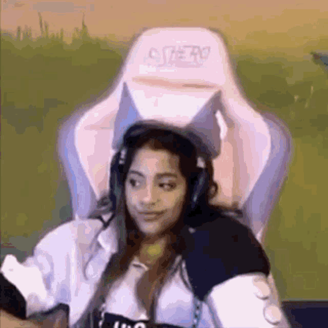 a woman is sitting in a pink gaming chair wearing headphones and smiling .