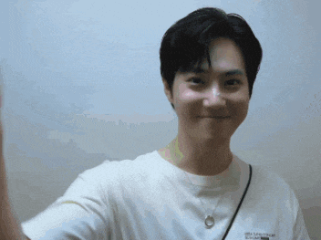 a young man wearing a white t-shirt with a necklace around his neck looks at the camera