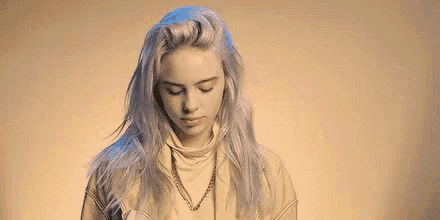 billie eilish is wearing a turtleneck sweater and a necklace .