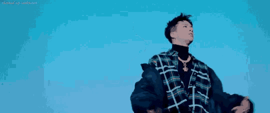 a young man wearing a plaid shirt and a black jacket is dancing in front of a blue sky .