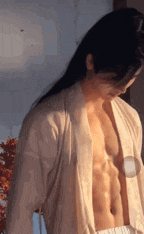 a man with long hair is standing in a room with his shirt off .