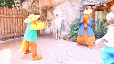 a man in a white shirt is standing in front of a fence with two mascots dancing in front of him .