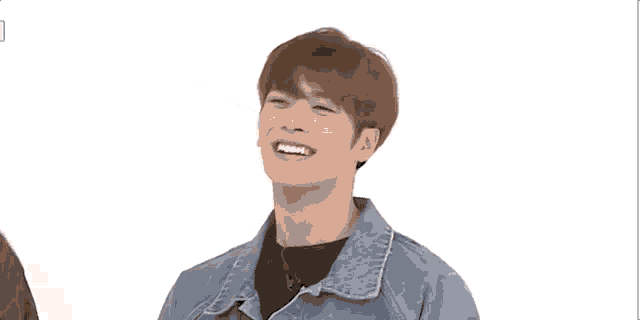 a young man wearing a denim jacket is laughing with his arms outstretched against a white background .
