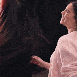 a woman in a pink sweater is smiling while standing next to another woman with long hair