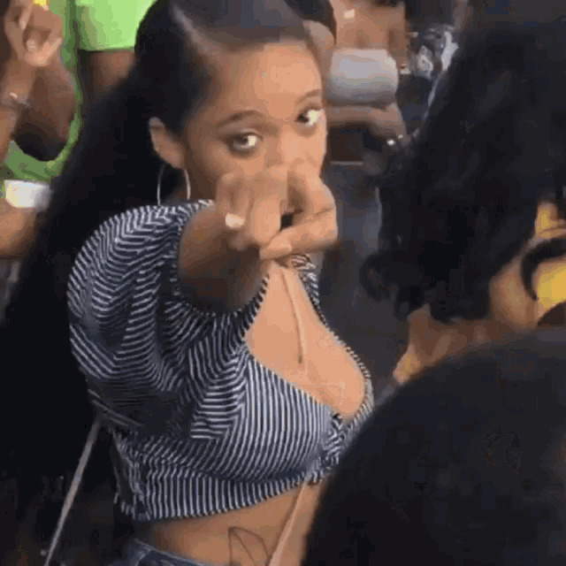 a woman in a striped crop top is pointing at someone in a crowd .