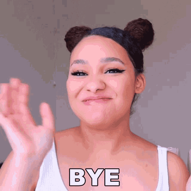 a woman with two buns on her head says bye with her hand