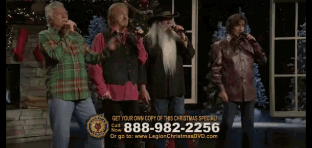 four men singing in front of a christmas tree with the number 888-982-2256