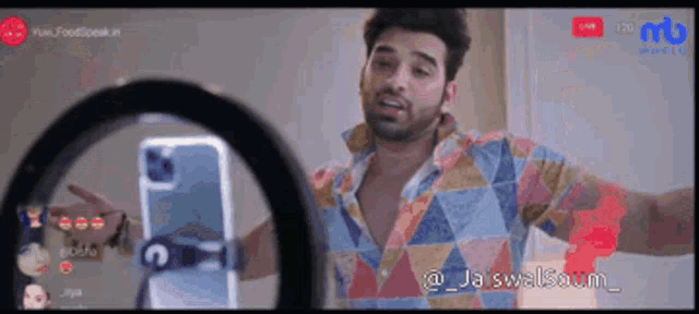 a man in a colorful shirt is taking a selfie with a ring light behind him