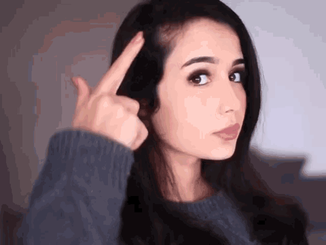 a woman in a grey sweater points to her hair