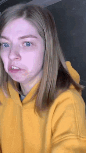 a woman wearing a yellow hoodie is making a face .