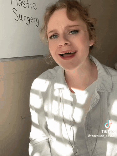 a woman is standing in front of a white board that says plastic surgery