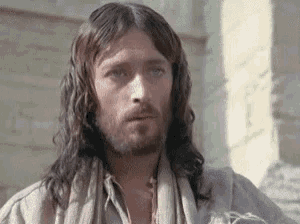 a man with long hair and a beard is standing in front of a brick wall .