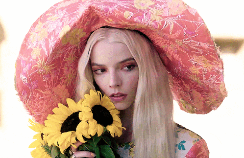 a woman wearing a large pink hat is holding sunflowers