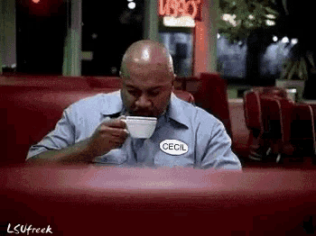 a man is sitting at a table drinking a cup of coffee .