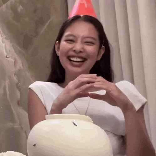 a woman wearing a red party hat is making a heart shape with her hands