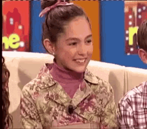 a girl in a floral jacket is smiling in front of a sign that says r