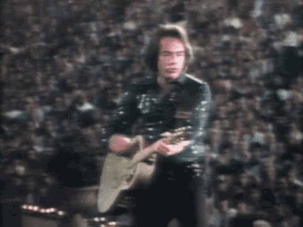 a man is playing a guitar in front of a crowd .