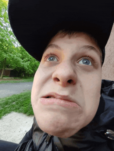 a man wearing a black hat and a black jacket makes a funny face
