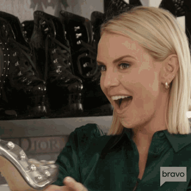 a woman in a green shirt is holding a silver shoe with a bravo logo in the corner