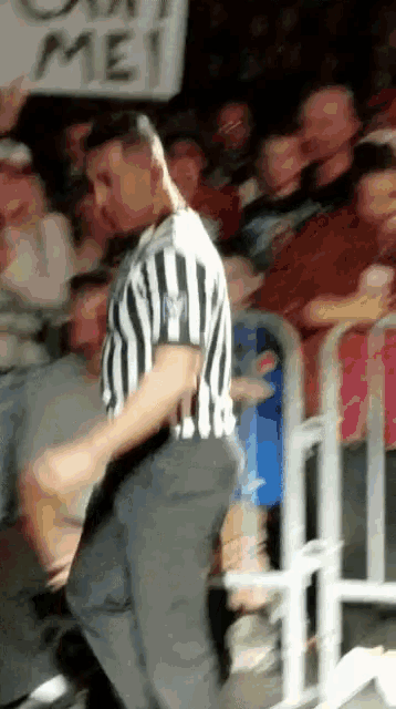 a referee in a striped shirt stands in front of a crowd with a sign behind him that says ' out men '