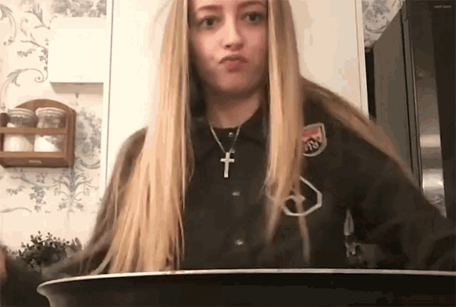 a woman with long blonde hair is wearing a black shirt with a cross on it