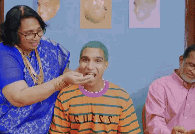 a woman is feeding a man a piece of cake while he wears a guess shirt