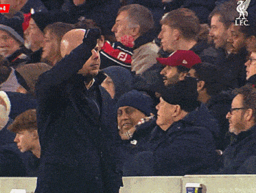 a man in a red hat with the liverpool logo on it stands in a crowd of people