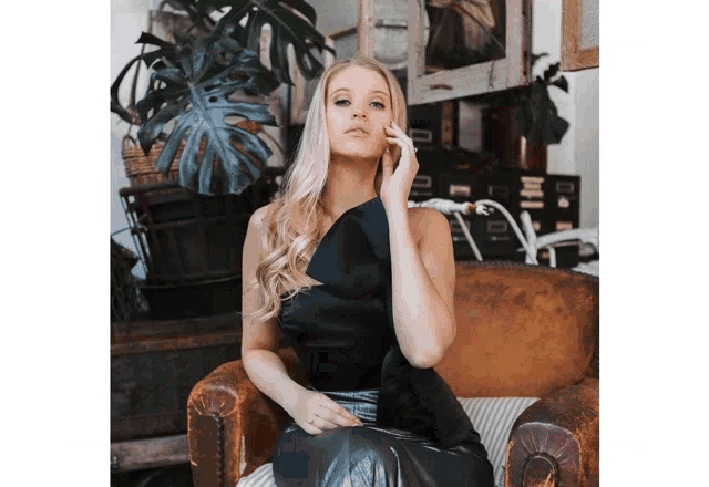 a woman in a black dress is sitting in a chair with her hand on her face