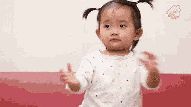 a little girl wearing a white shirt with polka dots is standing in front of a wall that says a home video