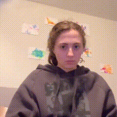 a woman wearing a grey hoodie with the word gap on it is standing in front of a wall with drawings on it .