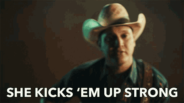 a man in a cowboy hat is playing a guitar with the words she kicks em up strong below him