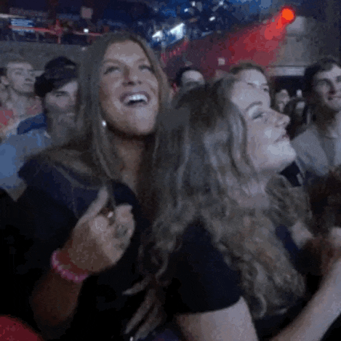two women are laughing in a crowd of people .