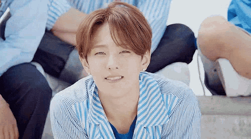 a young man in a blue and white striped shirt is smiling while sitting on a staircase .