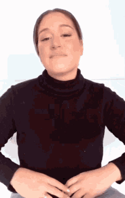 a woman wearing a black turtleneck sweater is holding her hands together .