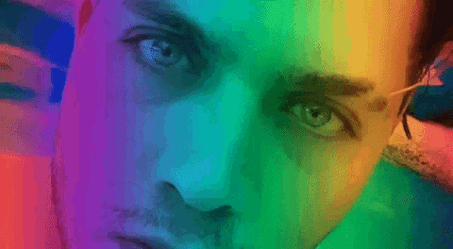 a close up of a man 's face with a rainbow of colors behind him