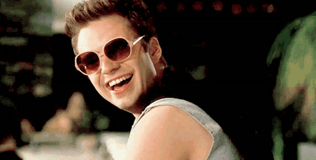 a man wearing sunglasses and a tank top is laughing