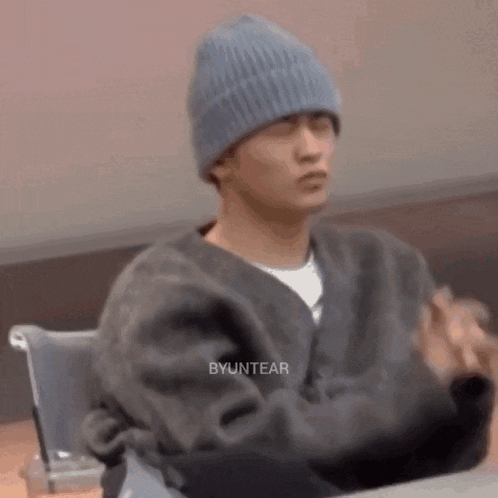 a man wearing a blue beanie is sitting at a table with his hands folded .
